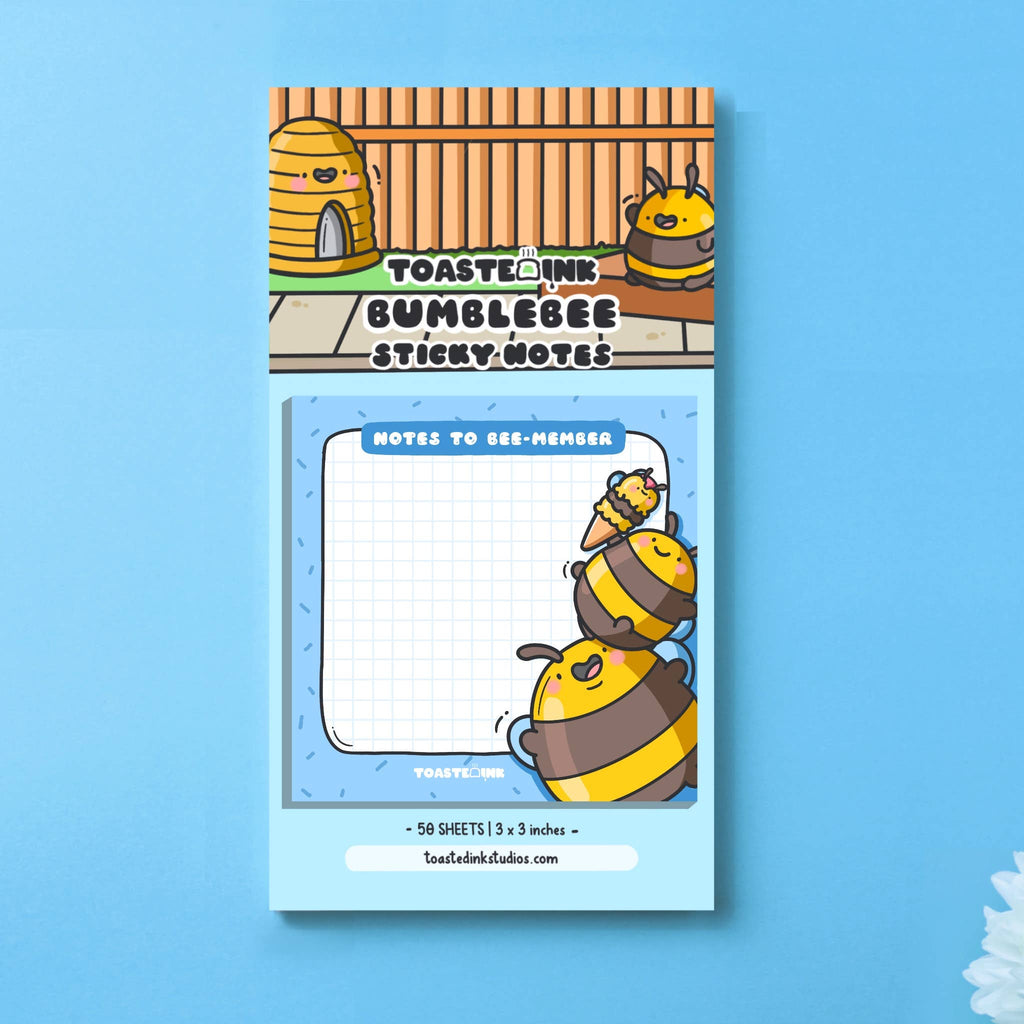 Square sticky note pad with a blue border and grid paper, featuring two chubby yellow and brown cartoon bumble bees stacking on top of each other to reach an ice cream. The top reads “Notes to Bee-member” in bold white text. Cute and practical stationery for daily reminders.