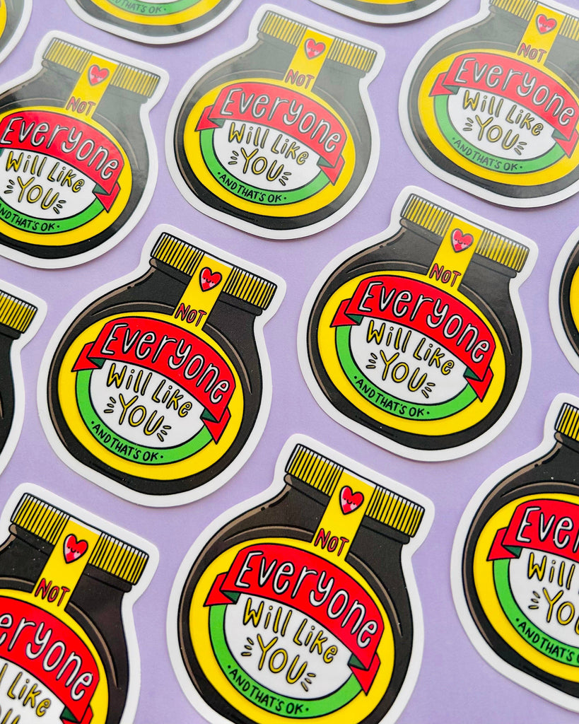 Multiple vinyl stickers laid out on a pastel purple background. Each sticker is shaped like a Marmite-style jar and reads: “Not Everyone Will Like You – And That’s OK.” Designed by Kellylou, sold by Rebel Romance, a small UK business selling alternative gifts and fashion.