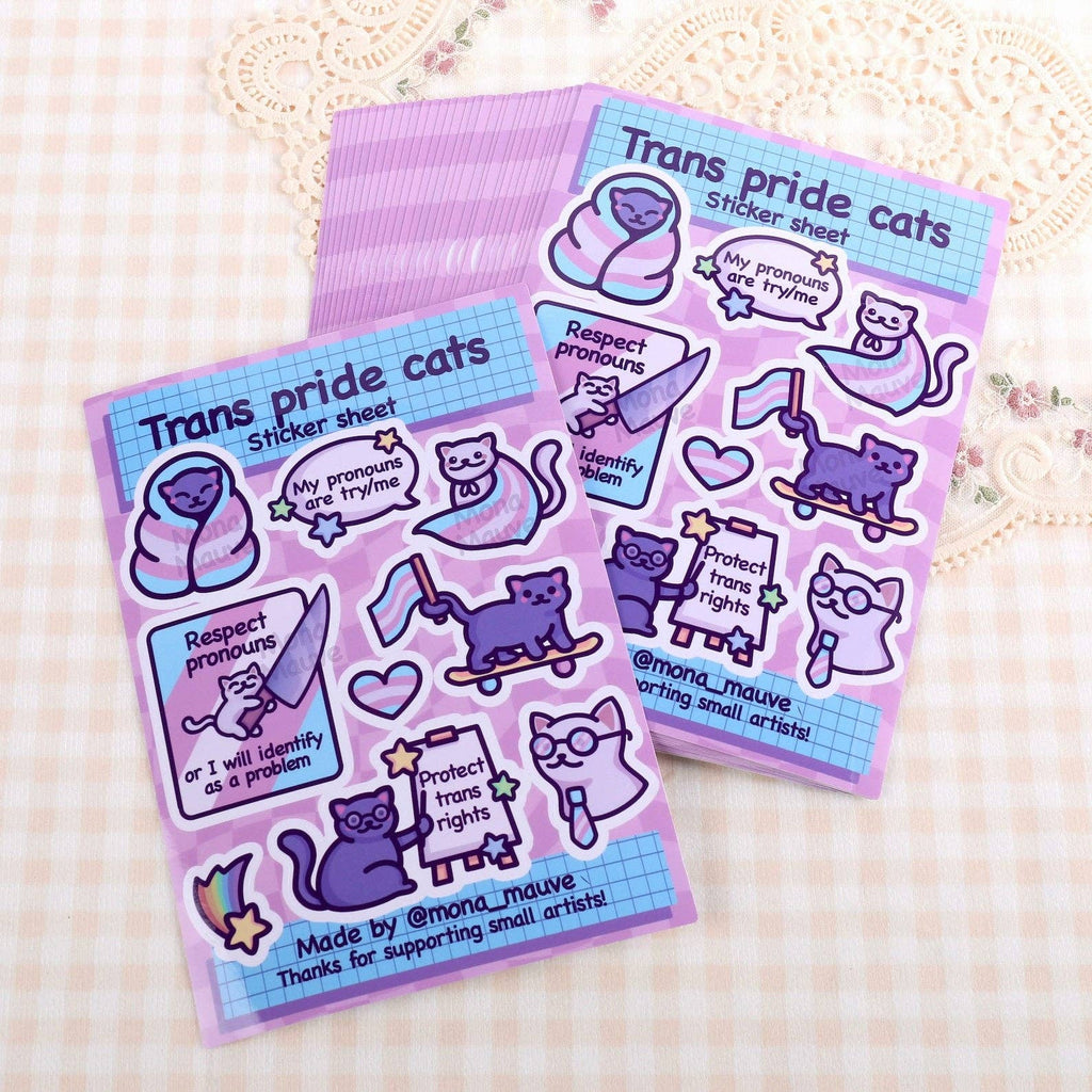 Two Trans Pride Cats Sticker Sheets by Mona Mauve, shown on a soft gingham and lace background. Includes 9 cute and waterproof vinyl stickers with affirming trans messages. Available at Rebel Romance, a small UK business that champions inclusivity, creativity, and alternative aesthetics for millennials.