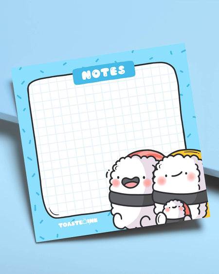 Fun and colourful sticky notes with cute sushi family characters and a grid layout. Styled flat-lay on a blue desk. From Toastedink, stocked by Rebel Romance UK.
