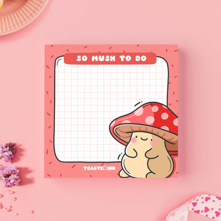 A square sticky note pad with a red border and grid paper design, featuring a cute, blushing mushroom character with a red and white spotted cap in the bottom right corner. The top header reads “So Mush To Do” in bold white text. A fun and functional memo pad for everyday reminders.