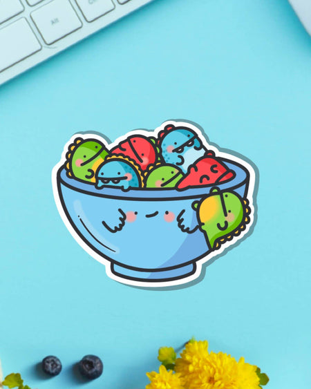 Toastedink’s colourful dinosaur bowl sticker on a pastel blue surface. Stocked by Rebel Romance, this playful waterproof vinyl sticker is a must-have for dino fans and lovers of cute, quirky designs.