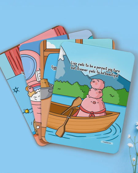 Close-up of Toastedink affirmation cards fanned out, including a pig family in a boat with the quote “Life fails to be a perfect pig-ture but it never fails to be beautiful.”