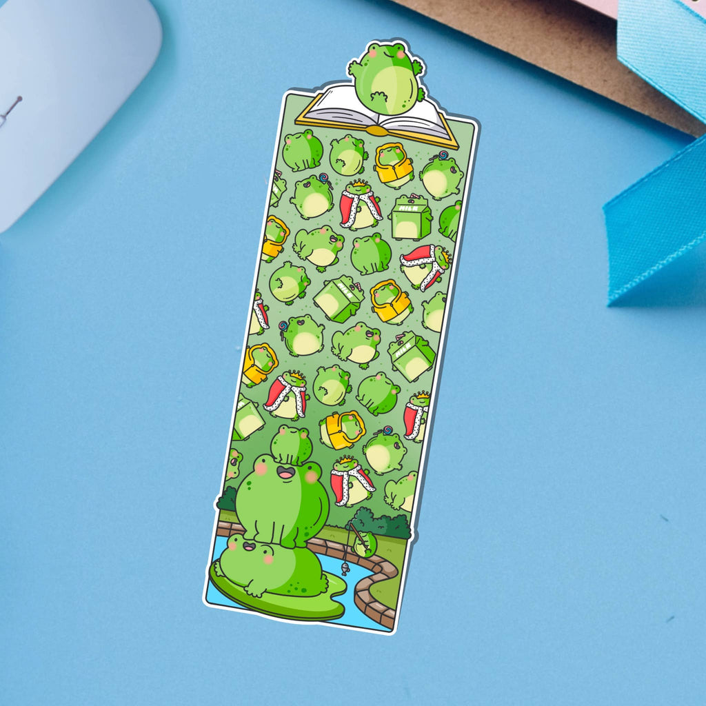 Glossy die-cut bookmark featuring a colourful pattern of cartoon frogs, drinks, books, and accessories on a green background. A frog sits atop an open book at the top, with more frogs stacked on a lily pad at the bottom.