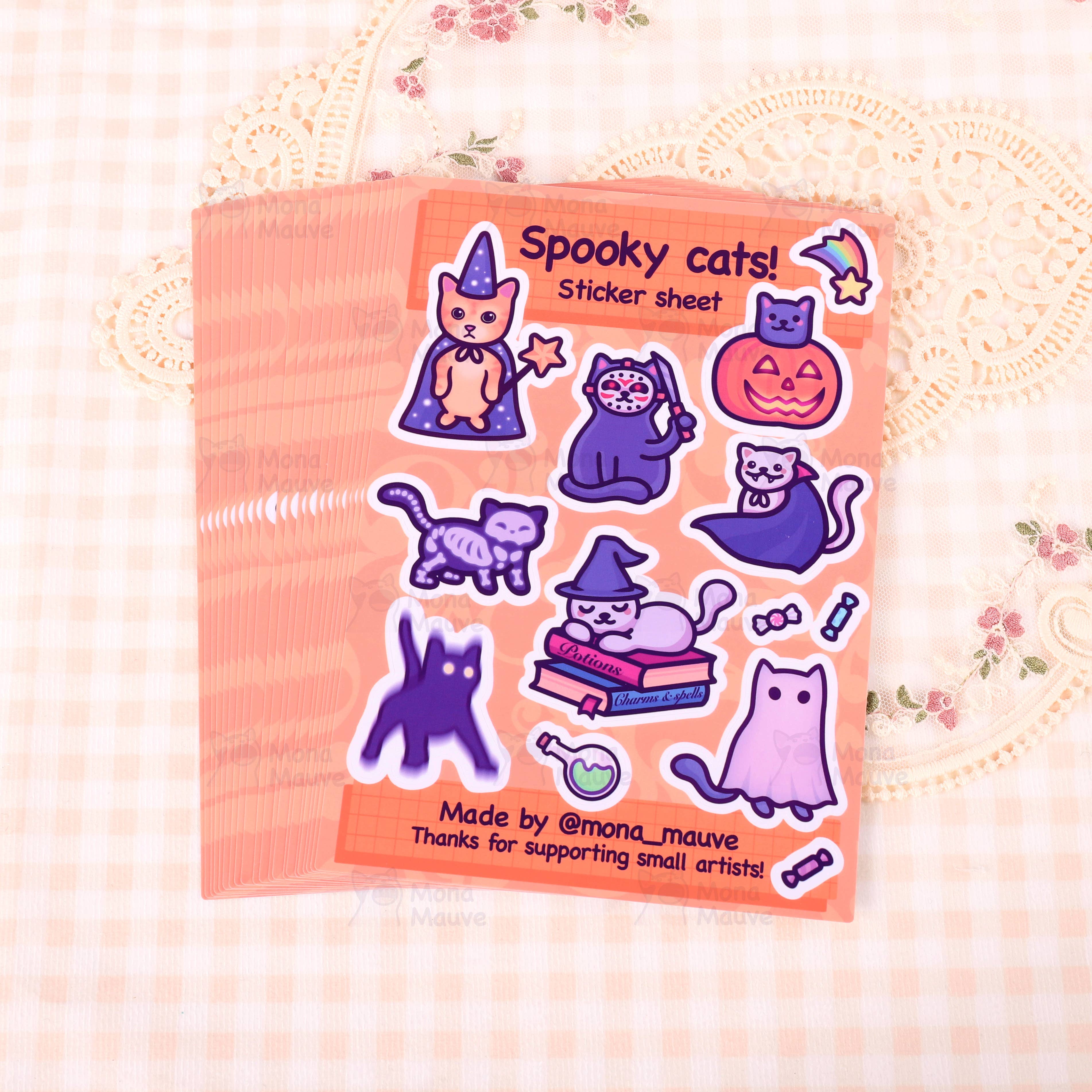Stack of Spooky Cats! Halloween Sticker Sheets by Mona Mauve, laid out on a soft, vintage-style checkered fabric. Each sheet includes 13 adorable vinyl stickers of spooky-themed cats and Halloween icons. A charming and fun gift for lovers of all things witchy, cute, and cat-related.