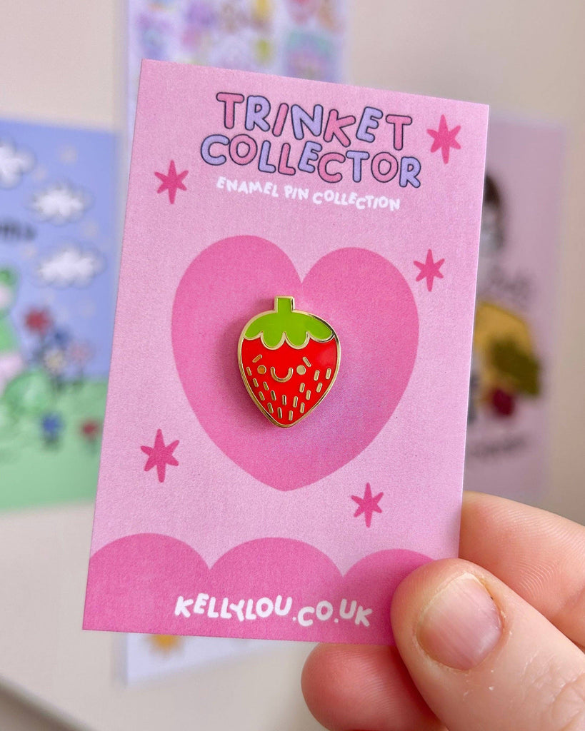 Close-up of the Berry Cutie Strawberry Mini Enamel Pin by Kelly Lou on a pink backing card with heart and star designs. Sold by Rebel Romance, a UK small business celebrating alternative style for millennials with quirky gifts, jewellery and ethical fashion.