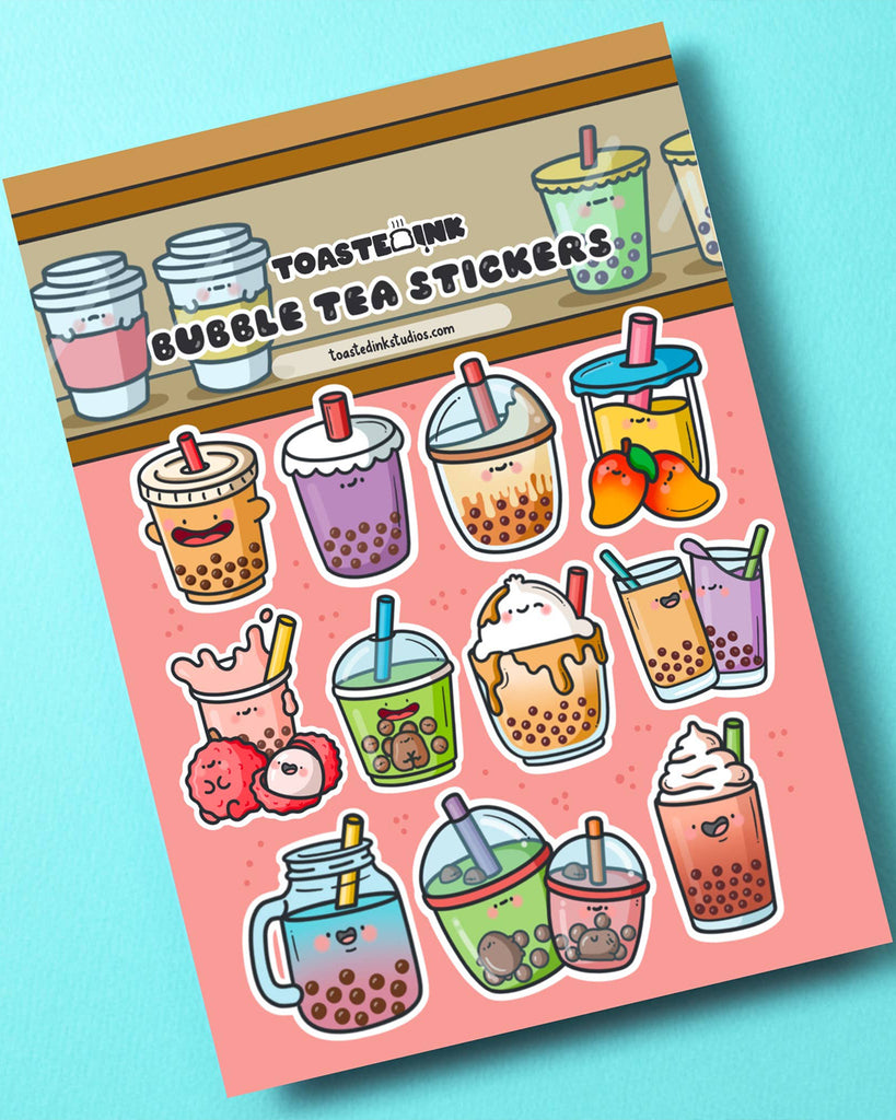 Flatlay of a Toastedink Bubble Tea Sticker Sheet from Rebel Romance on a blue background. The sheet includes 14 adorable illustrated boba drinks with happy expressions, colourful cups and fruit accents. Perfect for stationery lovers and kawaii fans.