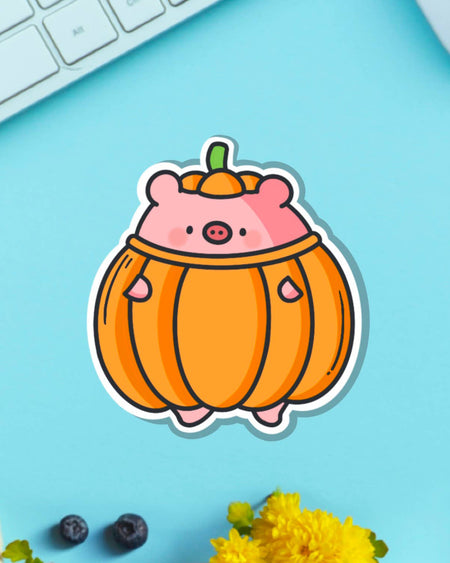 Pumpkin Pig vinyl sticker by Toastedink, sold by Rebel Romance. Features a kawaii pink pig inside a plump orange pumpkin costume. Displayed on a bright blue background with keyboard, flowers, and berries. Durable and glossy finish makes it ideal for decorating laptops or flasks.