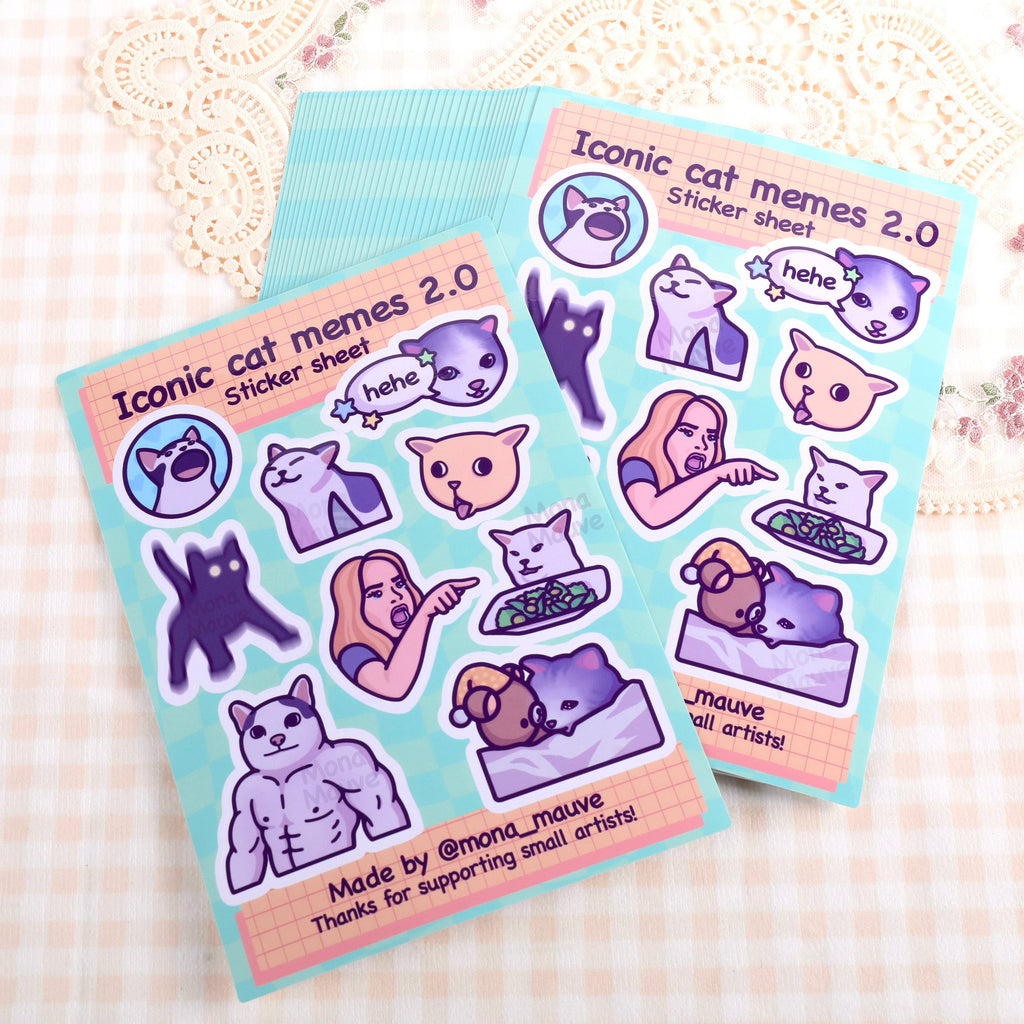 Two Iconic Cat Memes 2.0 Sticker Sheets by Mona Mauve placed on soft gingham fabric. Each sheet includes 9 humorous waterproof vinyl stickers featuring well-known cat memes in a cartoon style. A quirky, fun stationery item from a small independent artist perfect for decorating laptops, notebooks, or gifts.