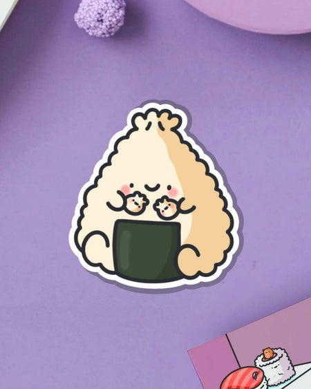 Toastedink’s happy dumpling onigiri vinyl sticker on a purple background. This cute character is holding mini dumplings and brings joy to any surface. A Rebel Romance fave for fans of quirky, foodie-themed accessories.