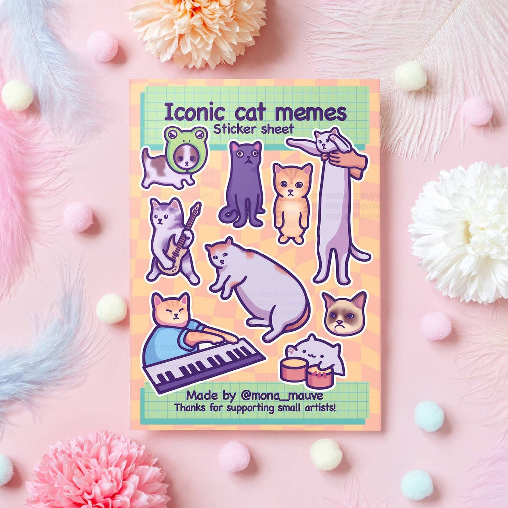 Flat lay of the Iconic Cat Memes Sticker Sheet by Mona Mauve, featuring 9 funny vinyl stickers of popular internet cat memes, including keyboard cat and long cat. Set on a pastel pink background with fluffy pompoms and flowers. A cute and quirky gift idea for cat lovers and meme fans.