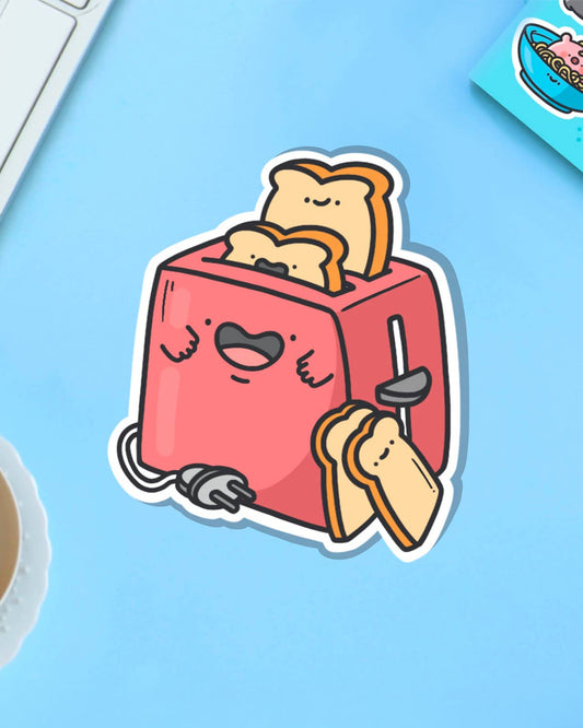Quirky toaster vinyl sticker from Toastedink, shown on a pastel blue background with a cup of tea and cereal bowl illustration nearby. Features a smiling red toaster with animated toast. Sold by UK brand Rebel Romance, celebrating weird and wonderful everyday magic.