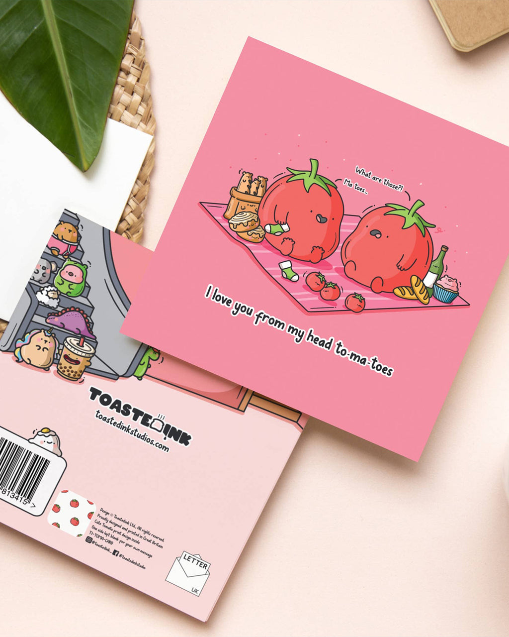 Flat lay of the 'I love you from my head to-ma-toes' greeting card on a light background. The back of the card shows the Toastedink logo and fun illustrations. Sold by Rebel Romance, a UK brand celebrating alternative and playful gifts.
