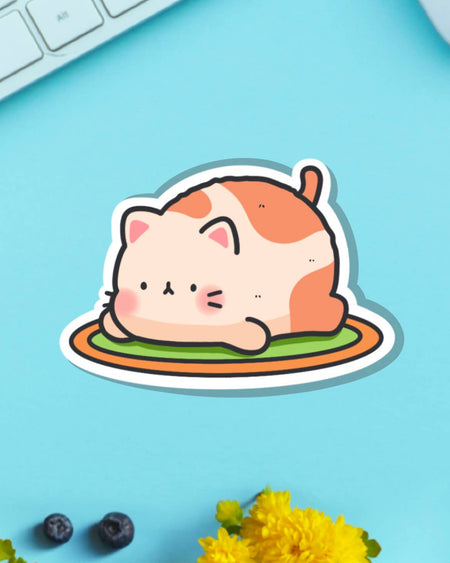 Resting Cat Vinyl Sticker by Toastedink, available at Rebel Romance. Features a cartoon-style orange and cream cat lying flat on a striped rug. The sticker is shown on a pastel blue background with blueberries and yellow flowers. Perfect for adding cute vibes to your laptop or planner.