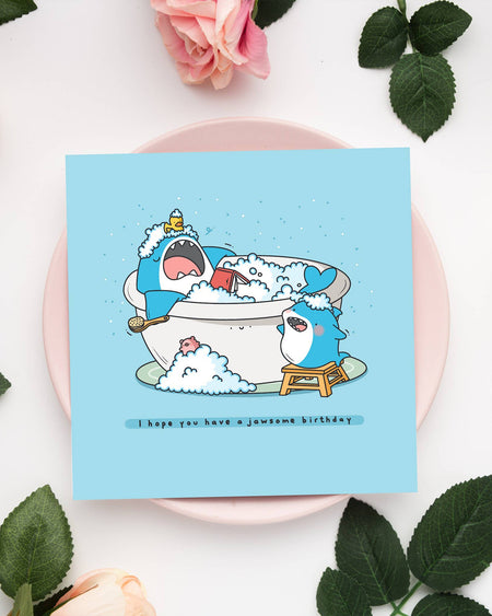 Birthday card featuring two cartoon sharks in a bubble bath, surrounded by roses. Caption reads "I hope you have a jawsome birthday." A cute and pun-filled card by Toastedink, available from Rebel Romance.