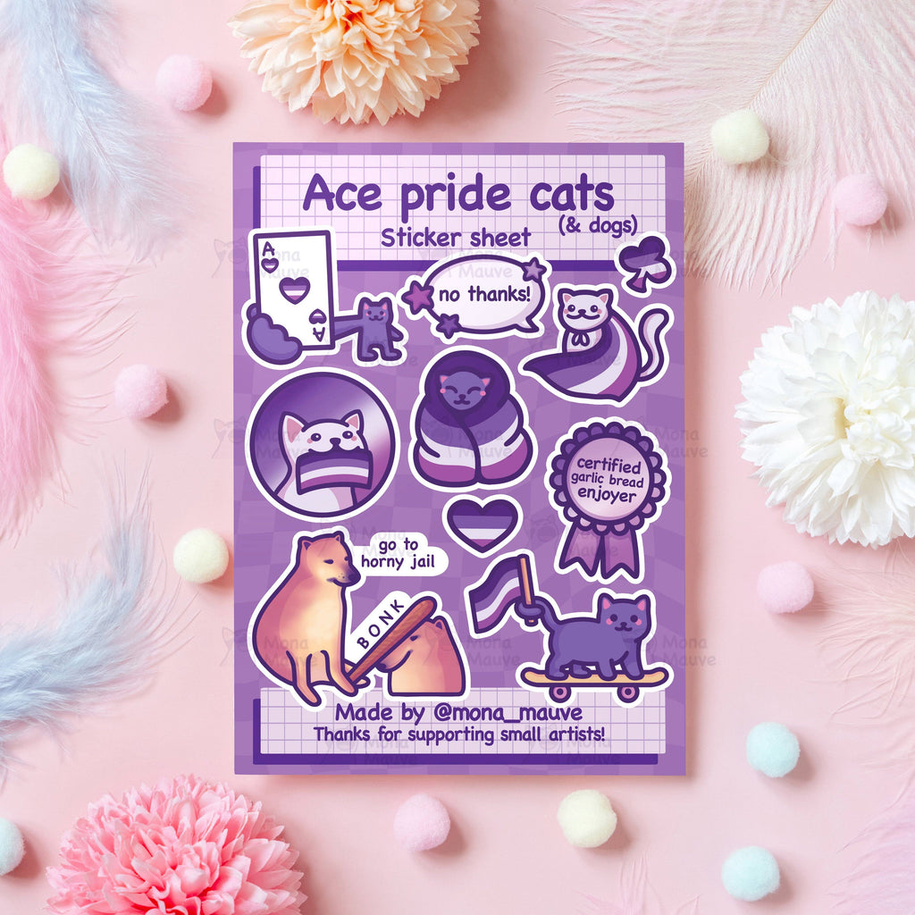 A flat lay photo of a purple sticker sheet titled “Ace pride cats (& dogs)” by Mona Mauve, surrounded by pastel flowers, pompoms, and feathers on a pink background. The sheet includes 10 cute vinyl stickers of cats and dogs with asexual pride themes—like a wrapped-up cat, a cat holding an ace playing card, and a dog bonking another dog with a bat that says “BONK.” One sticker reads “certified garlic bread enjoyer.”