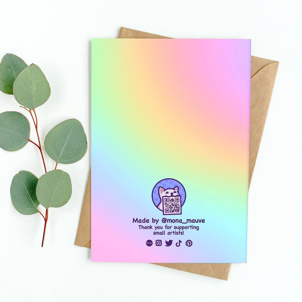 Back of the pastel rainbow coming out card designed by Mona Mauve for Rebel Romance. Includes a cute cat logo with a QR code and message: “Made by @mona_mauve – Thank you for supporting small artists!” Social media icons are shown along the bottom. The card is displayed with a kraft brown envelope and eucalyptus leaves.