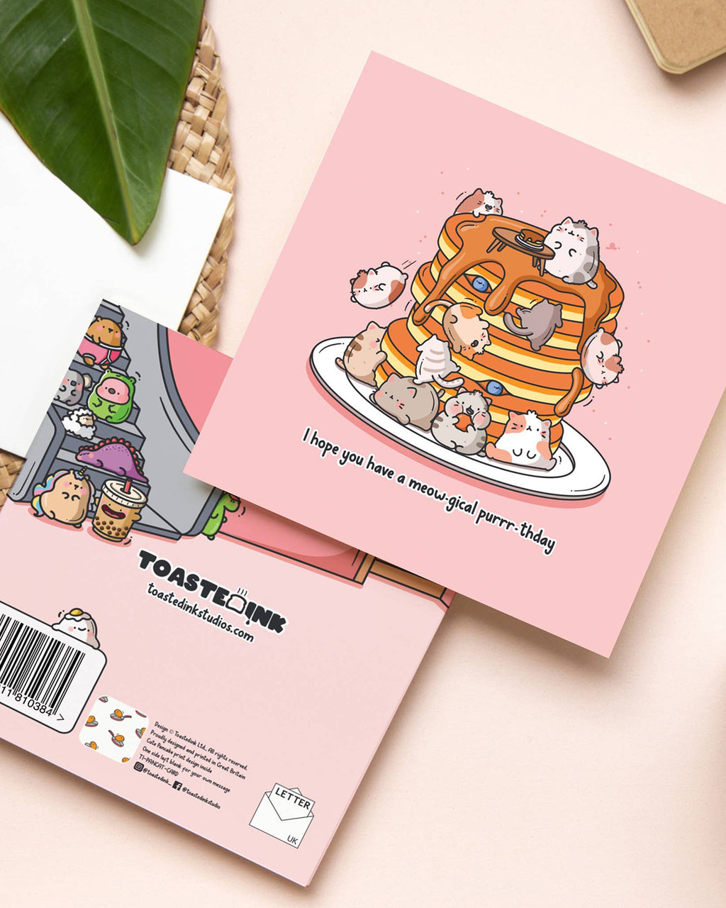 A square pink birthday card featuring cartoon cats lounging on a stack of syrup-drenched pancakes with the pun “I hope you have a meow-gical purrr-thday.” Shown next to the illustrated back cover featuring more cute characters. Sold by Rebel Romance, a UK small biz stocking quirky, retro-style designs for alternative millennials.