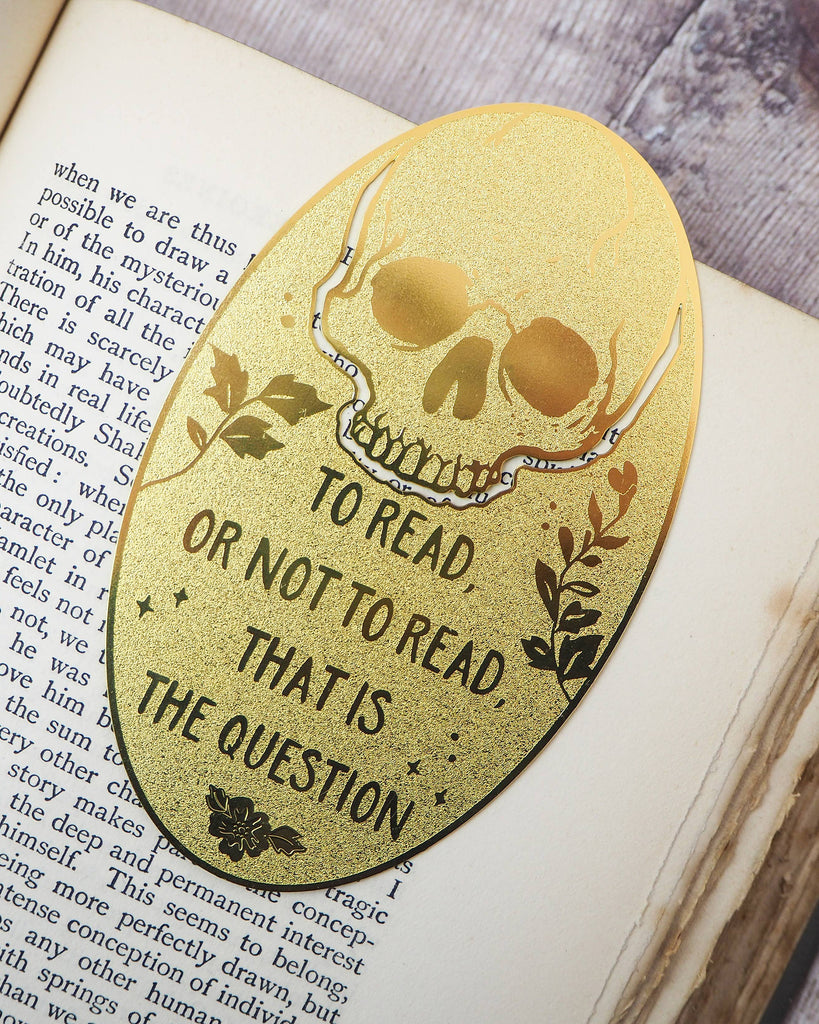 Shakespeare Hamlet Skull Brass Bookmark with skull and foliage detail engraved with “To read or not to read, that is the question”, resting in an open book. Sold by Rebel Romance, UK alternative brand.