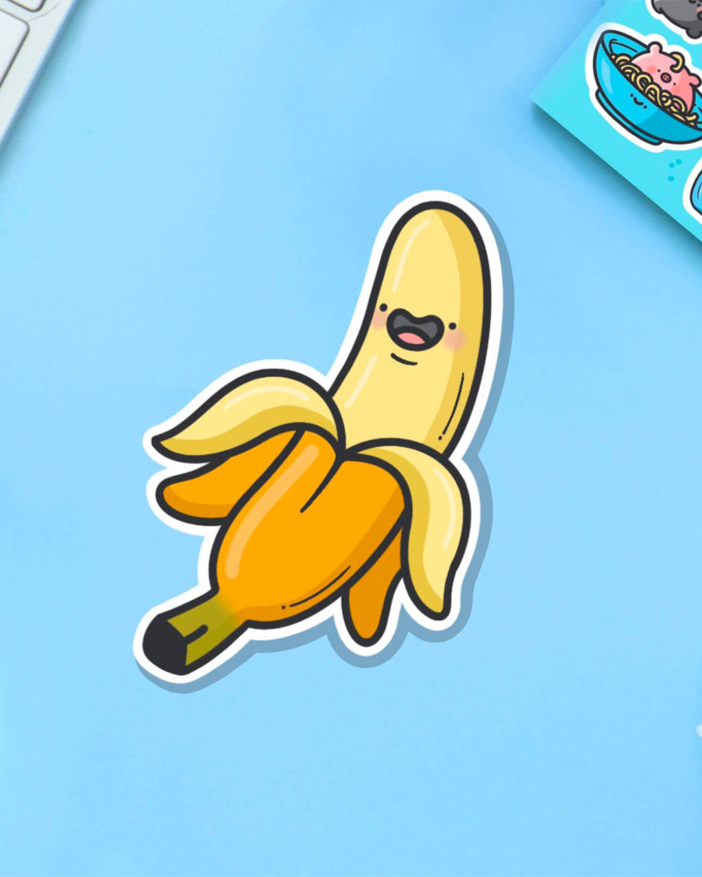 A-peel-ing banana sticker by Toastedink, sold by Rebel Romance, printed on waterproof vinyl. Shown on a light blue backdrop next to other cute character stickers.