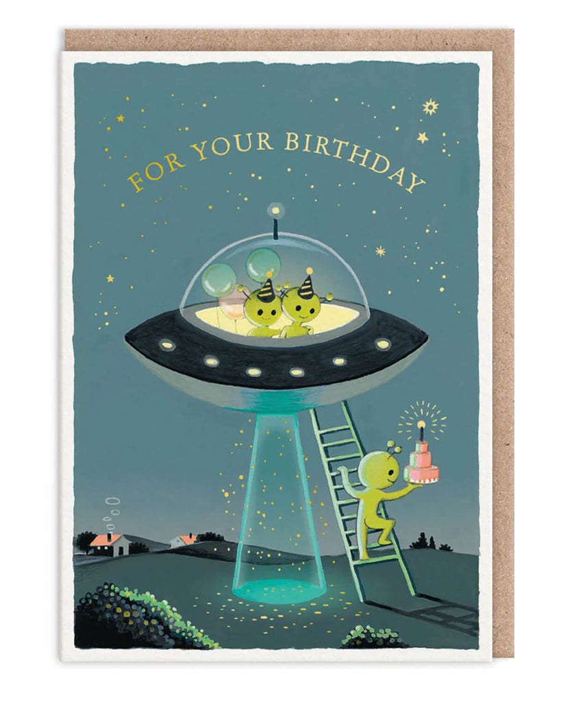 Quirky birthday card from Rebel Romance featuring cute green aliens in a UFO. One alien carries a pink layered birthday cake up a ladder into the spaceship, where two other aliens in party hats wait with balloons. Set against a night sky with stars, this playful card is perfect for space lovers and fans of alternative style. Ideal for millennials who love fun, offbeat gifts and unusual greetings.