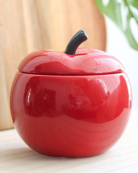 Close-up of the Red Apple Ceramic Oil Burner on a light wooden surface, with a plant in the background.