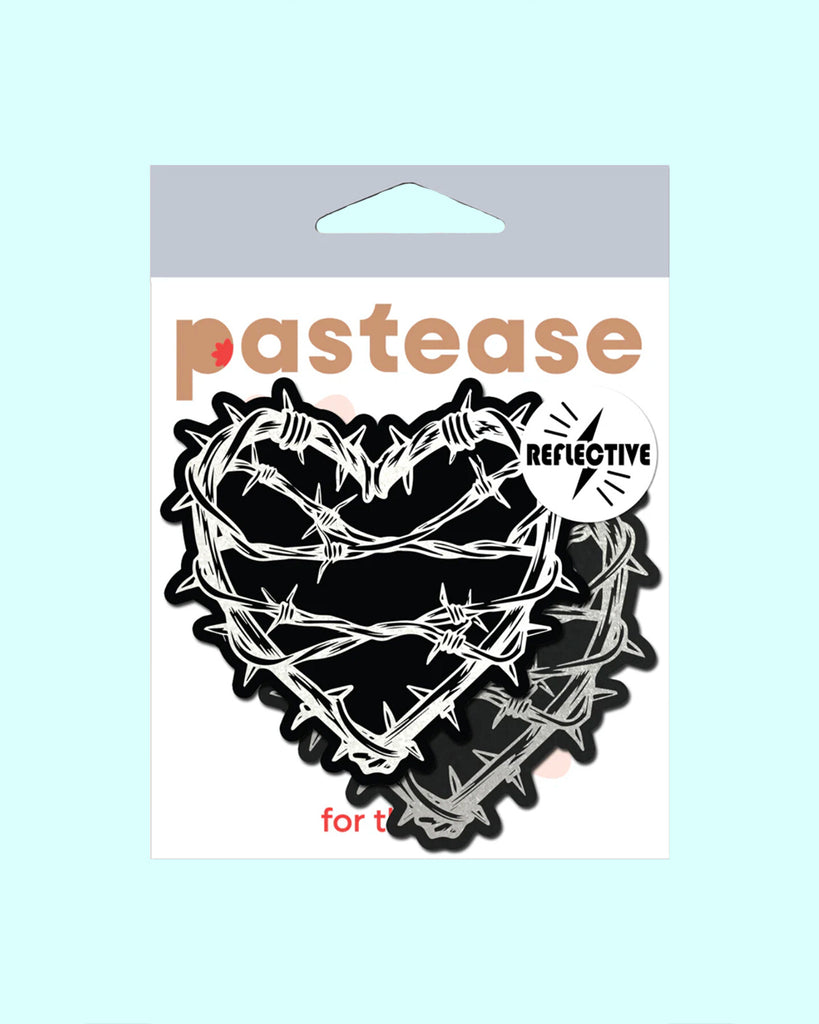 The Barbed Wire Heart Pasties Reflective Nipple Covers by Pastease®. Two black hearts with silver reflective barbed wire patterned shaped nipple covers shown in the pastease pastel packaging on a pastel blue background. Perfect for festivals, pride, burlesque, raves, only fans content or parties.