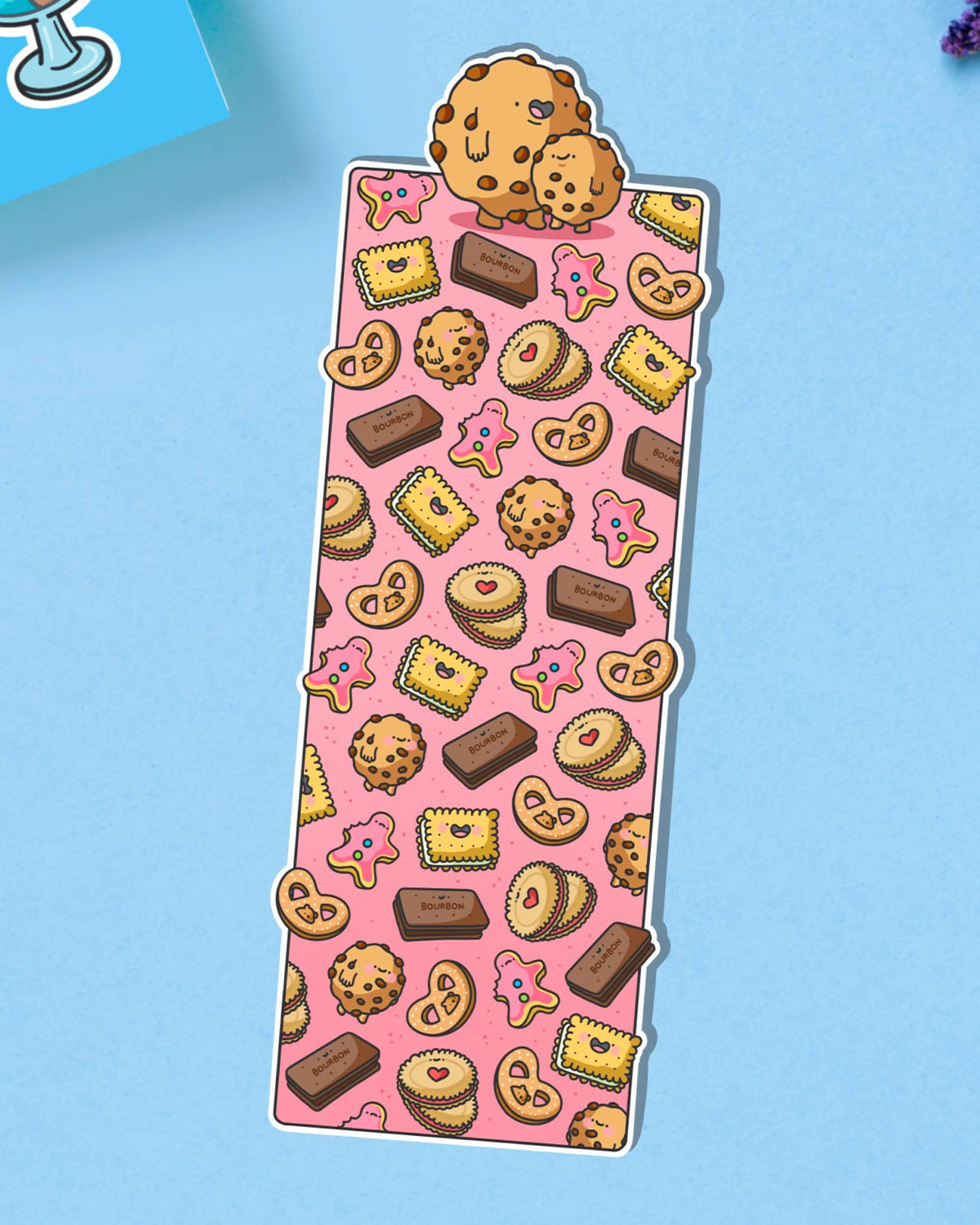 Glossy biscuit-themed bookmark featuring cartoon illustrations of cookies, pink iced biscuits, bourbons, jammy dodgers and other treats on a pink background. Topped with two cute chocolate chip cookies.
