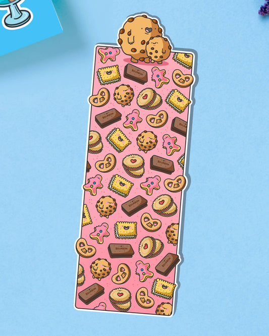 Glossy biscuit-themed bookmark featuring cartoon illustrations of cookies, pink iced biscuits, bourbons, jammy dodgers and other treats on a pink background. Topped with two cute chocolate chip cookies.
