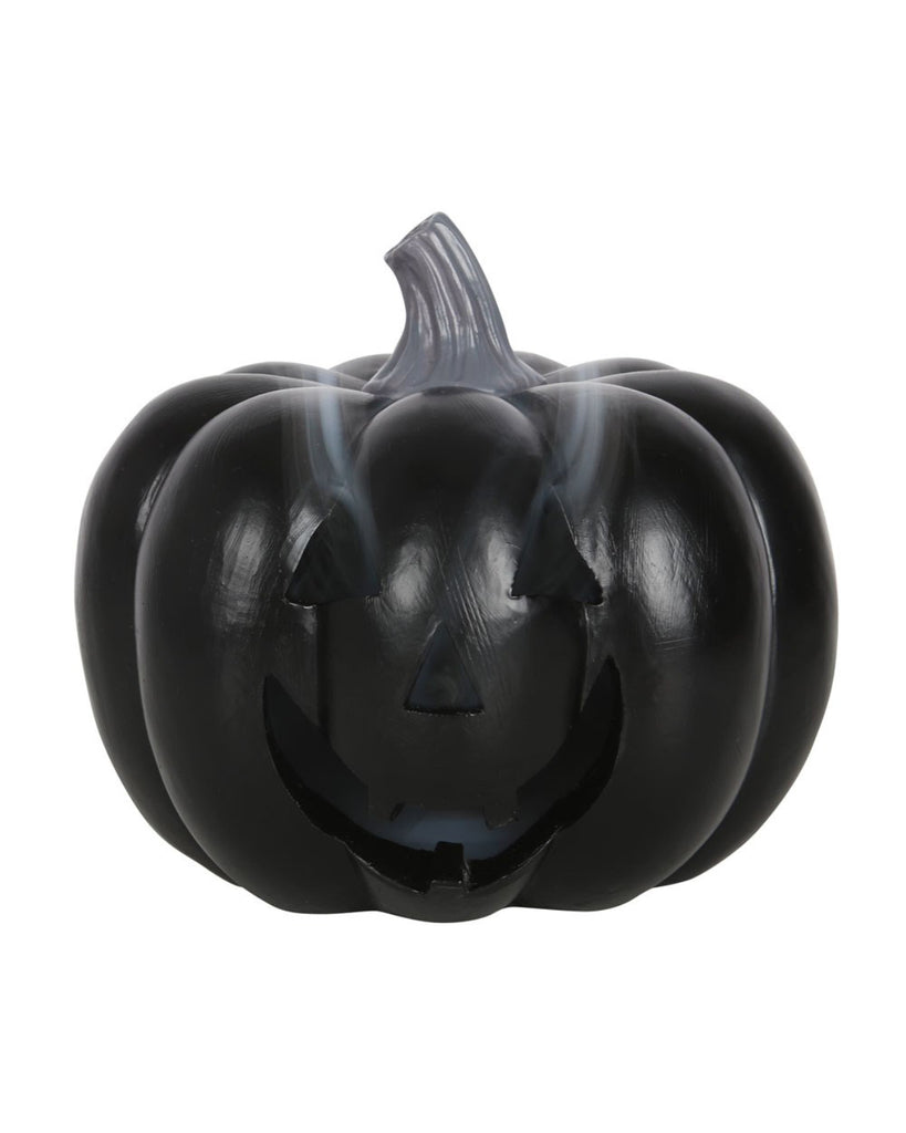 A black pumpkin-shaped incense cone holder with a carved jack-o’-lantern face, releasing trails of fragrant smoke from its eyes and mouth.