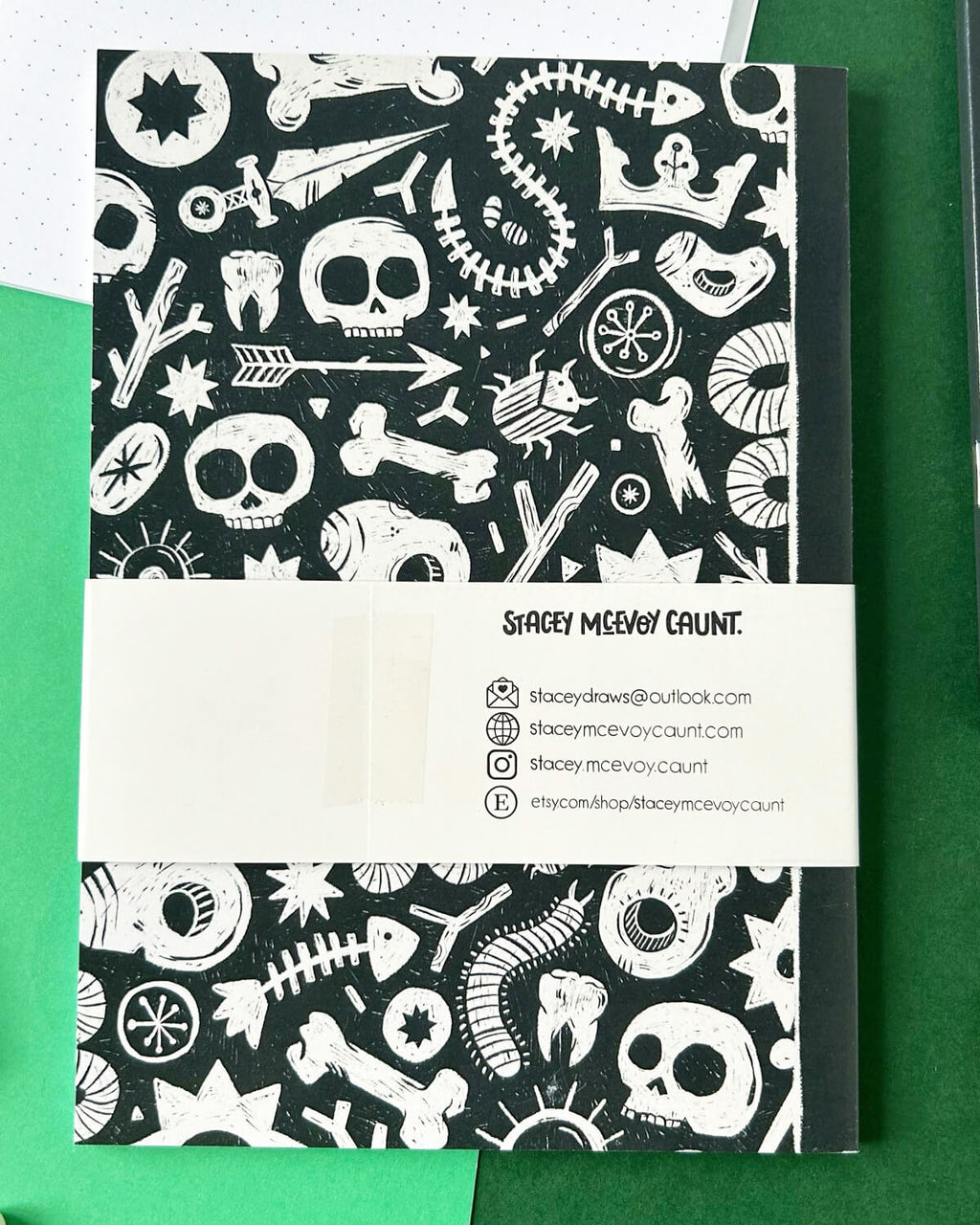 Back view of the journal, showing the same detailed pattern with bones, stars, and arrows, along with the designer’s contact information on a white wrap-around band.