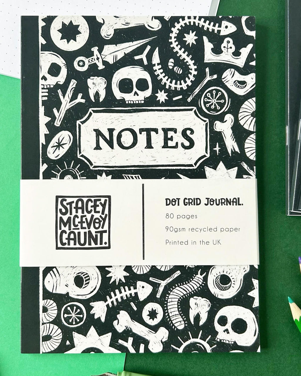 Full view of the front cover, showcasing the intricate black and white design with skulls and bones and the text “Dot Grid Journal - 80 pages, 90gsm recycled paper, Printed in the UK” on the band.