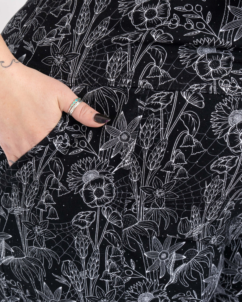 Detailed close-up of a front pocket on the Rebel Romance Black Floral Cobweb Stretch Dungarees. The white cobweb and botanical print on black stretch fabric creates a striking gothic aesthetic.