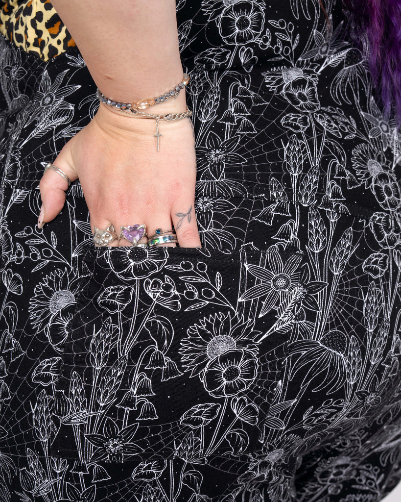 Close-up of the back pocket on the Rebel Romance Black Floral Cobweb Stretch Dungarees, highlighting the intricate monochrome floral and cobweb print, paired with Luisa’s silver rings and bracelets for added style.