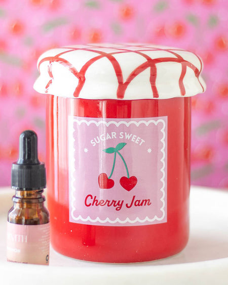  Close-up of the cherry jam jar oil burner, highlighting its glossy finish, red and white lattice lid, and pastel pink label with cherries.