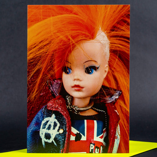 Punk-themed card featuring a retro doll with bright orange mohawk hair, a punk jacket, and a Union Jack shirt, set against a bright yellow and black background.