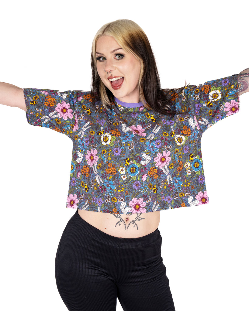 Florence stretches out her arms showing the front of the Rebel Romance Cottagecore Cropped Boxy Tee. The enchanted print features pastel flowers, buzzing bees, and fluttering dragonflies. A dreamy slow fashion top with a meadow-core feel.