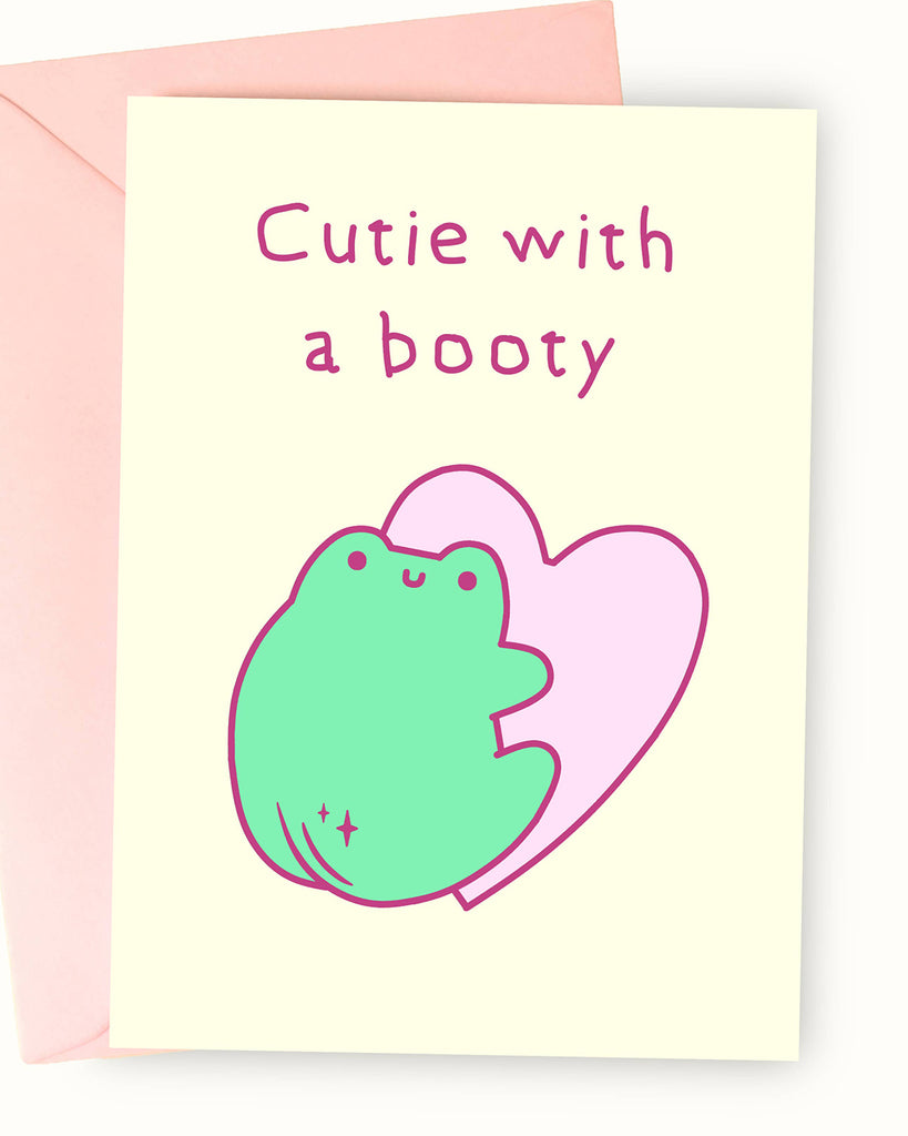 A pastel yellow greeting card featuring a cute green frog illustration by Nimbob. The frog has a round body, tiny happy face, and a cheeky peach-like booty with sparkles. Behind the frog is a soft pink heart outline. The text reads ‘Cutie with a booty’ in a playful handwritten font. A fun and flirty card, perfect for a loved one or a special someone with a great sense of humour!