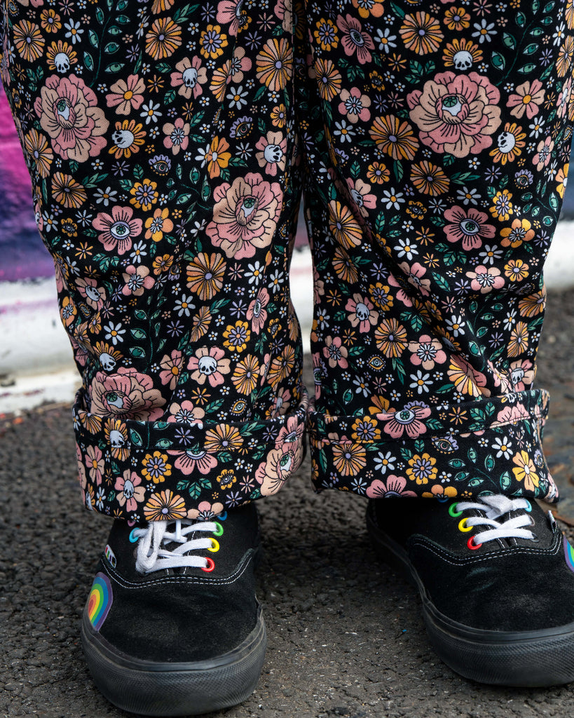 Close-up of the Eye Spy Floral Dungarees fabric showing detailed pink and mustard flowers with mystical eyes and skull motifs on black stretch twill.