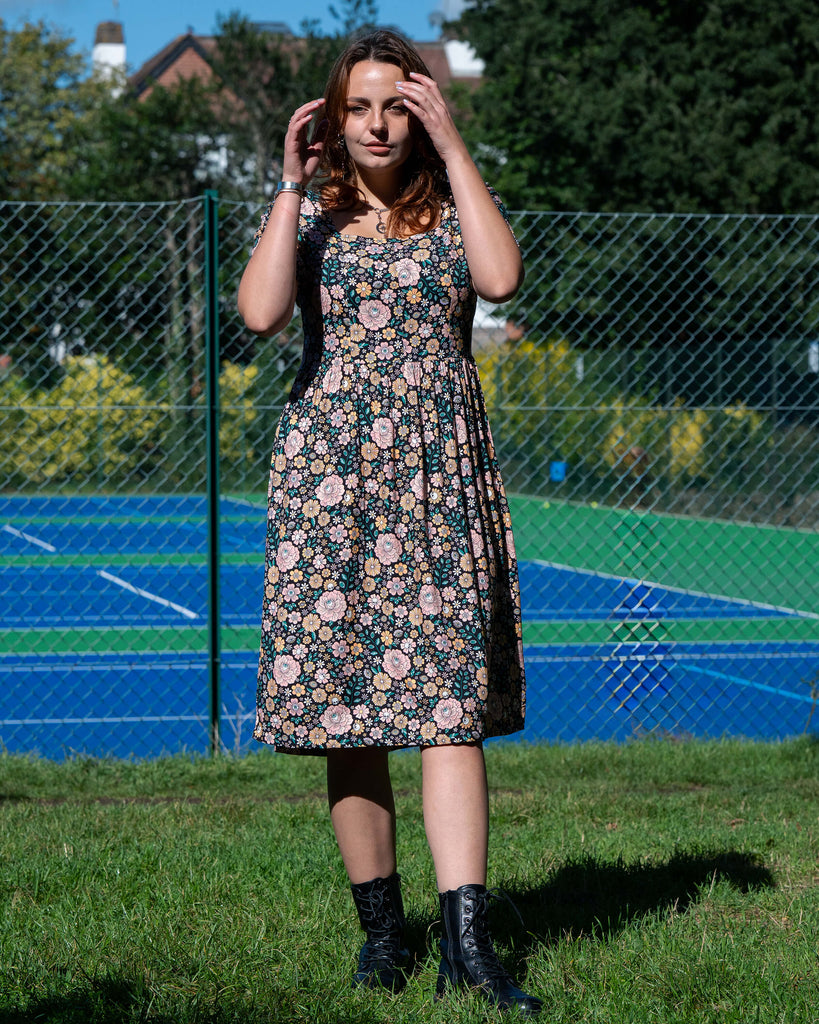 Woman in a floral dress standing outdoors with a tennis court in the background