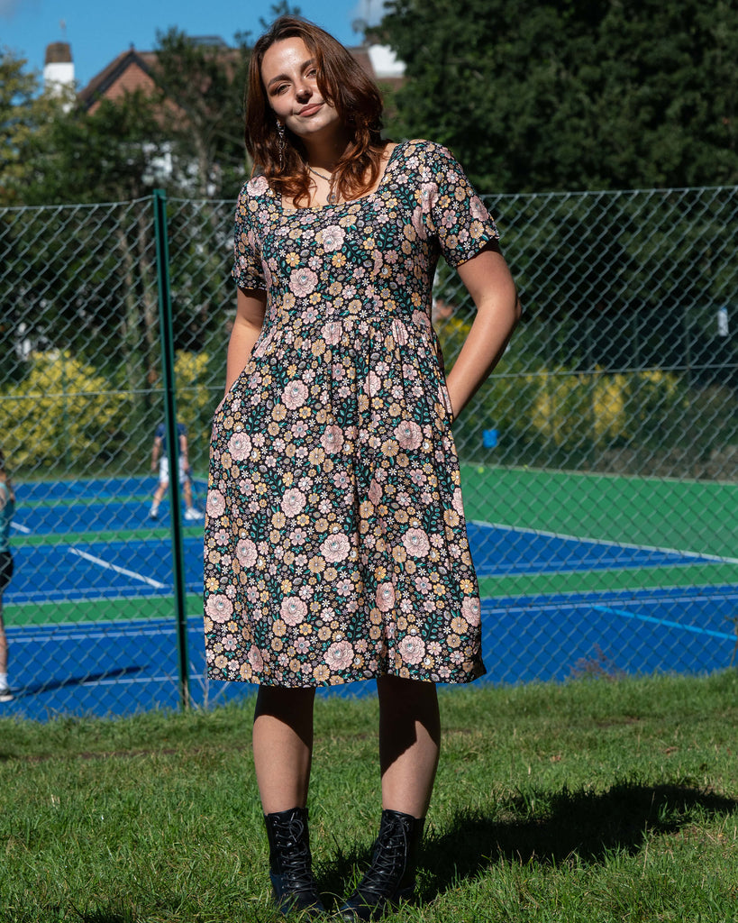 Woman in a floral dress standing on grass with a tennis court in the background