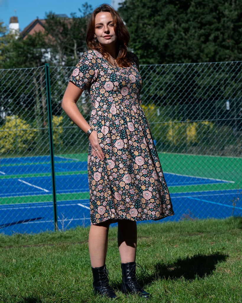 Woman in a floral dress standing on grass with a tennis court in the background