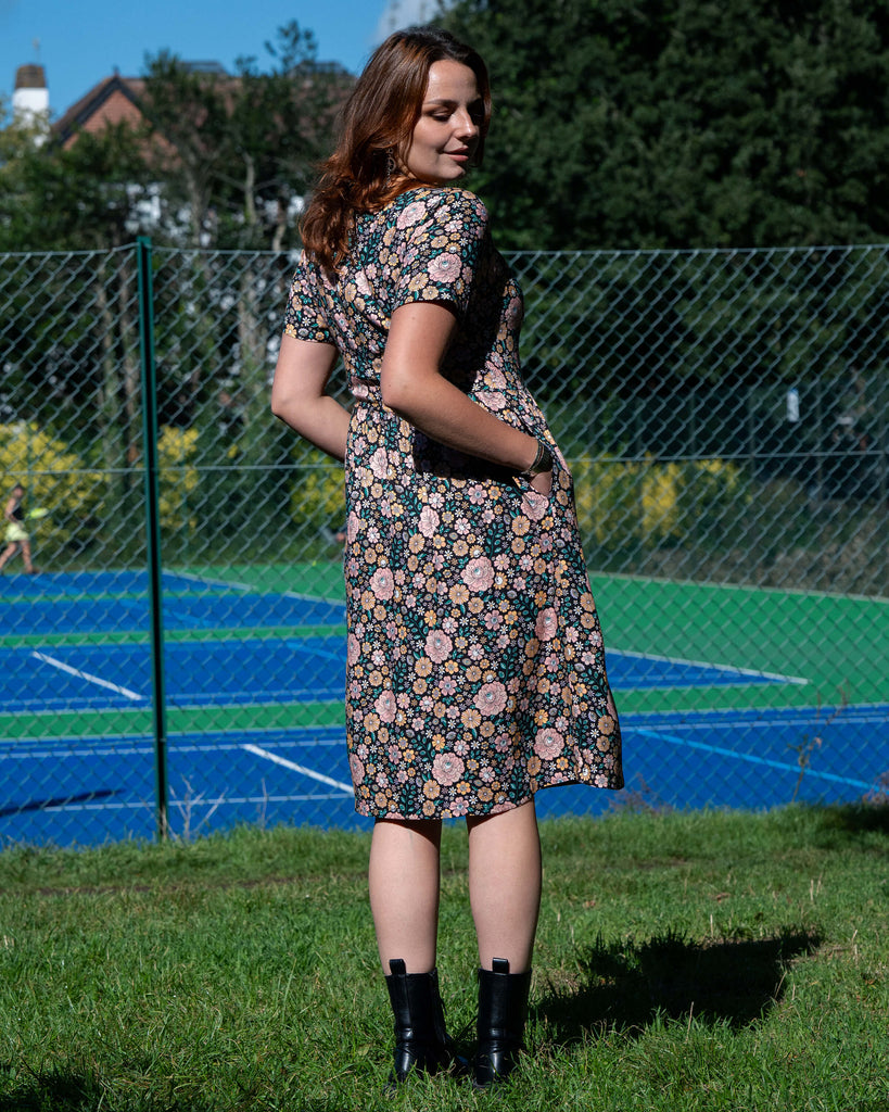 Woman in a floral dress standing outdoors with a tennis court in the background