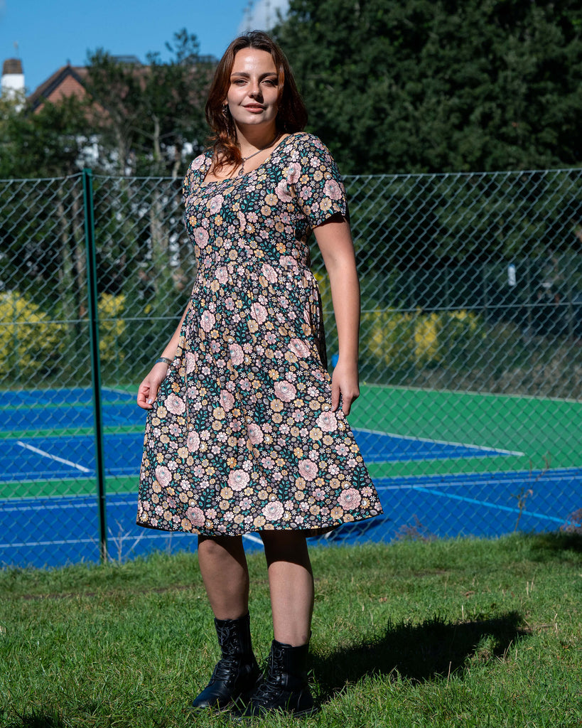 Woman wearing a floral dress standing outdoors with a tennis court in the background
