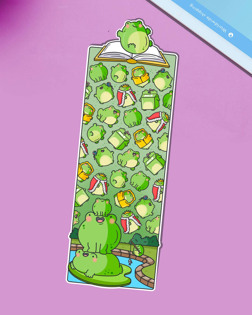 Glossy die-cut bookmark featuring a colourful pattern of cartoon frogs, drinks, books, and accessories on a green background. A frog sits atop an open book at the top, with more frogs stacked on a lily pad at the bottom.