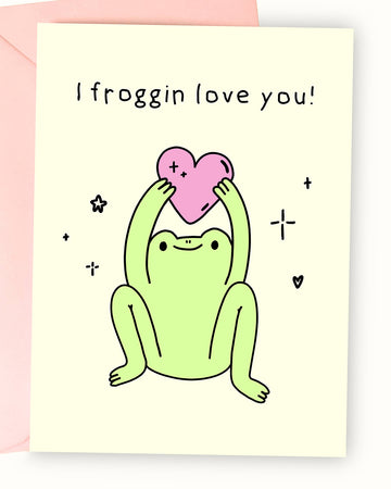 A pastel yellow greeting card featuring an illustration by Nimbob of a happy green frog sitting with its legs spread and arms raised, holding a pink heart. The frog has a cute, content expression, surrounded by sparkles, tiny hearts, and star doodles. The text above reads ‘I froggin’ love you!’ in a playful, handwritten font. A fun and wholesome card, perfect for friendships, anniversaries, or Valentine’s Day.