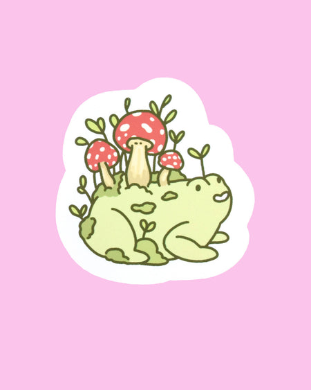 A vinyl sticker featuring a hand-drawn illustration by Nimbob of a happy, chubby green frog with tiny sprouts and red mushrooms growing from its back. The frog has a joyful expression, surrounded by soft earthy tones. The sticker has a white border and is perfect for decorating laptops, notebooks, and more. A cute and whimsical design for nature lovers and frog fans alike!