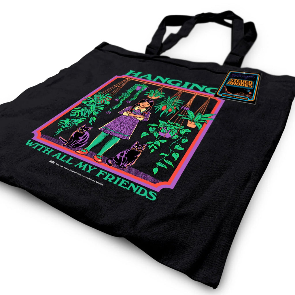 A black tote bag featuring Steven Rhodes’ “Hanging With All My Friends” design. The artwork shows a young girl in a purple dress and green tights standing with two black cats amidst lush hanging plants and greenery. The text reads “Hanging With All My Friends” in bright green lettering.