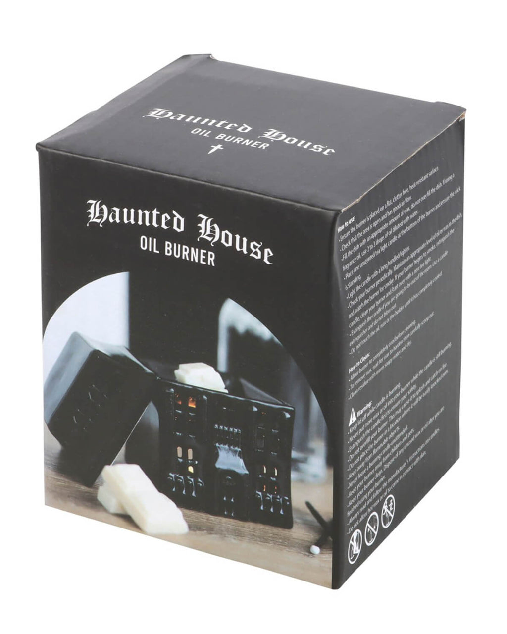 A black ceramic haunted house oil burner with intricate window and door cutouts, placed on a rustic wooden surface with wax melts scattered nearby.
