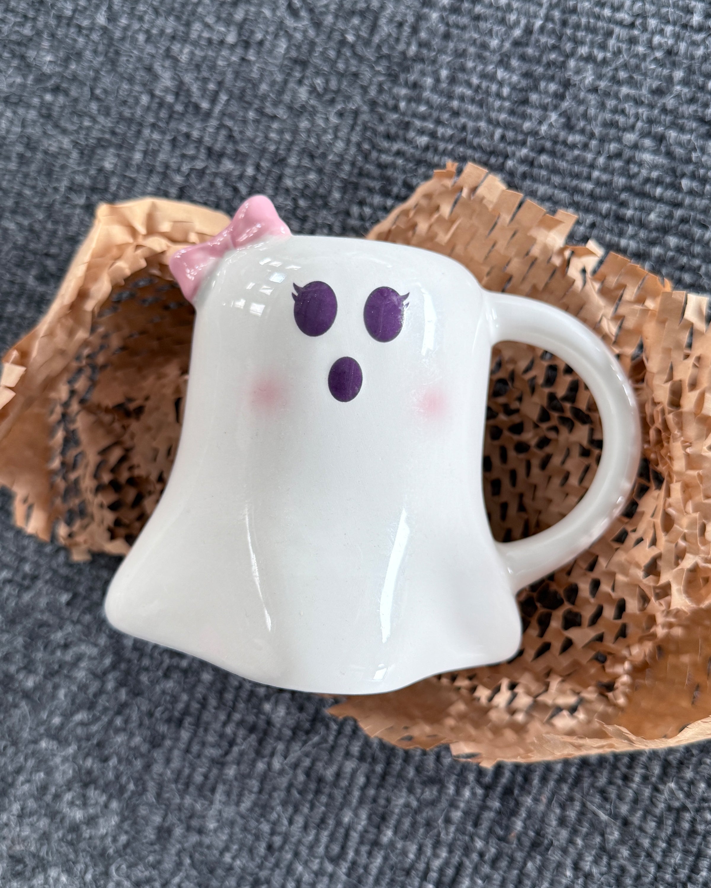 Mrs Boo Ghost Shaped Mug with Bow from Rebel Romance, a small UK brand celebrating alternative style and homeware. This cute ceramic ghost mug features big purple eyes, rosy cheeks, and a surprised expression, topped with a pastel pink bow. A perfect gothic yet playful gift for millennials who love quirky mugs, Halloween aesthetics, and unique homeware treasures.
